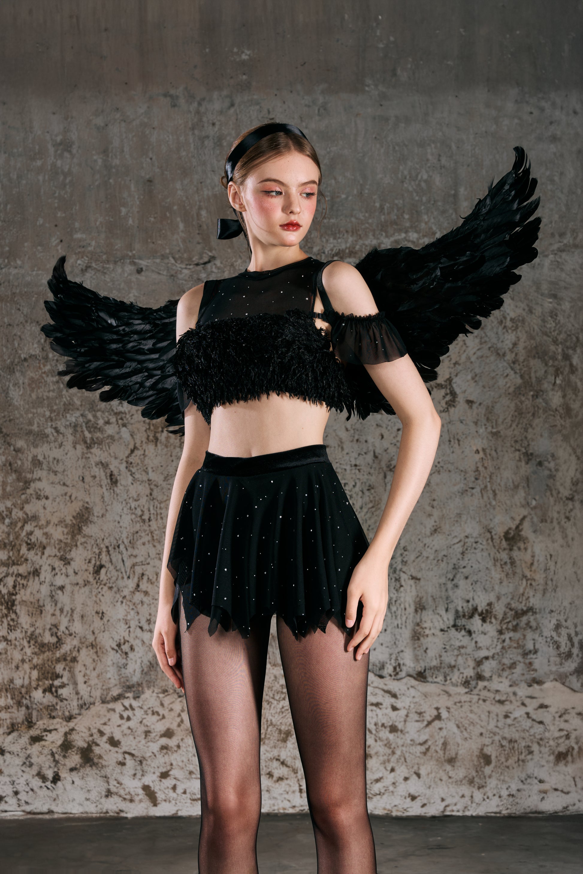 Model wearing a black outfit with feathered wings against a textured wall Hebe designed by Spincess Pole Dance Aerial Ballet Dance wear